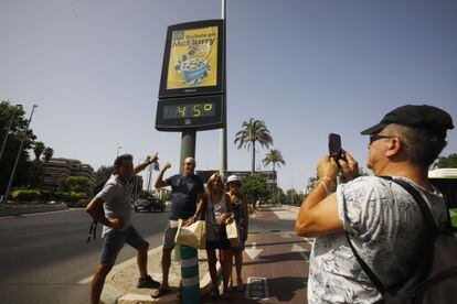 Unos turistas se fotografían debajo de un termómetro de calle que marca 45 grados, este jueves en Córdoba.