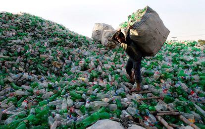 Un empleado de una factoría de reciclaje sobre un depósito de envases de plástico vacío en Lahore (Pakistán).
