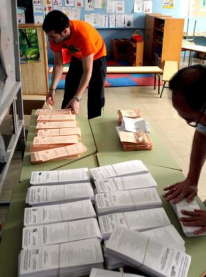 Varias personas en un colegio electoral de Bilbao colocan los sobres y las papeletas para el 22-M.