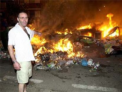 Un vecino de Málaga señala los contenderos incendiados en protesta por la huelga de limpieza.