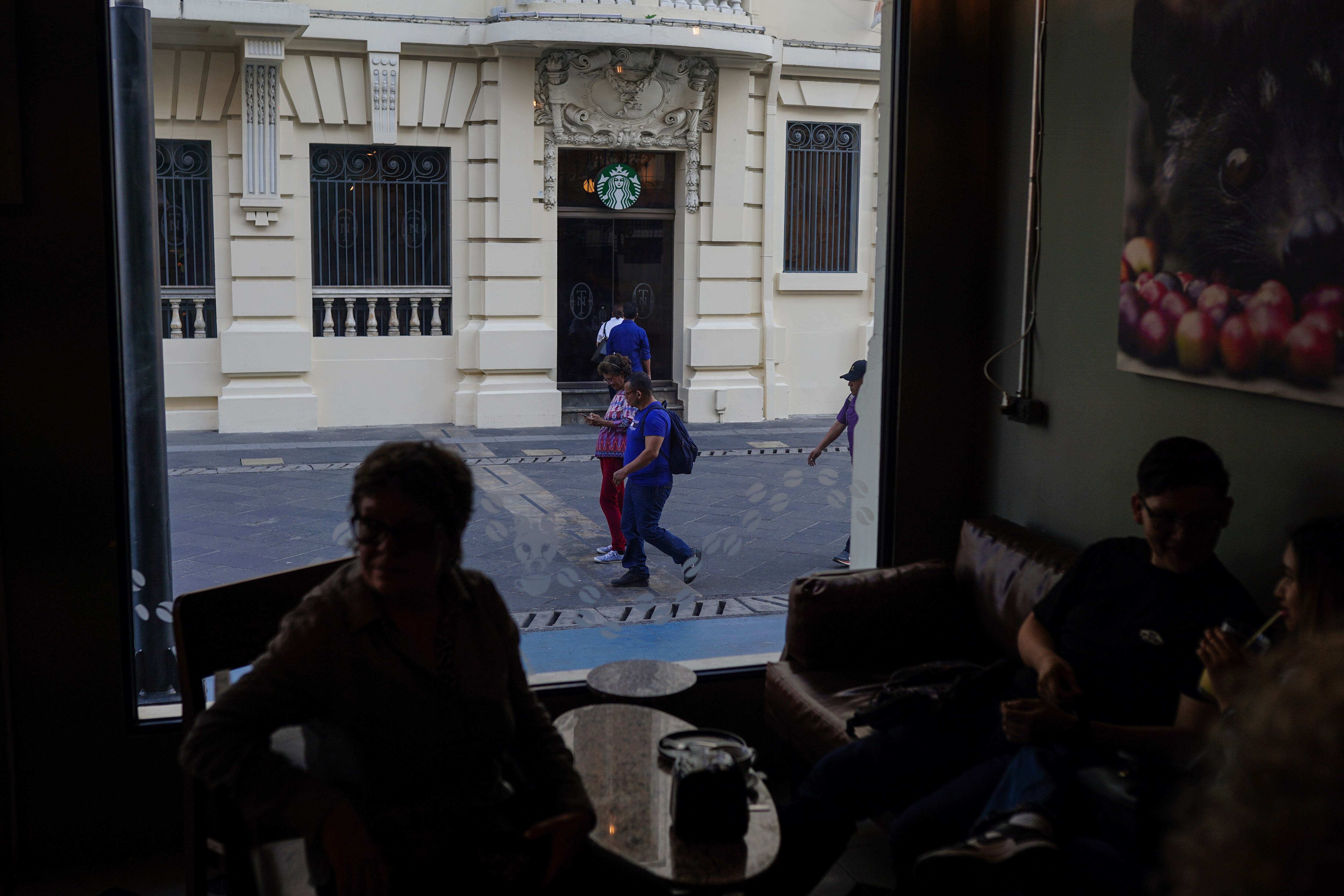 Clientes disfrutan de un café mientras peatones cruzan una calle remodelada de la capital salvadoreña.