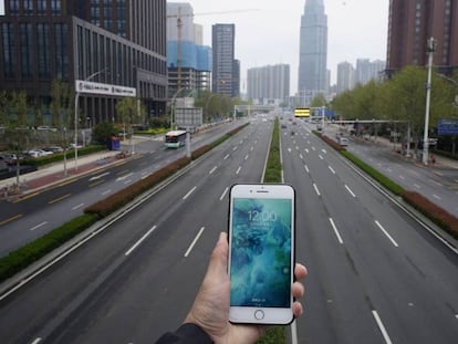 Una persona sostene un teléfono móvil frente a una carretera casi vacía en Wuhan.