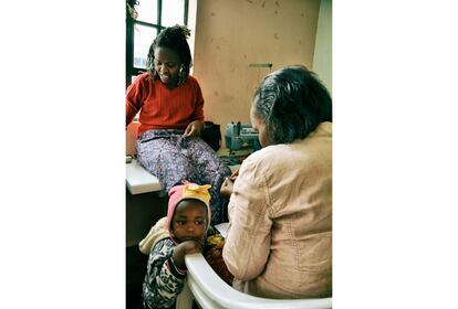 El pequeño Kimansi espera paciente mientras su madre práctica diseños con cuentas de colores.