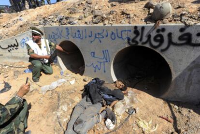 Combatientes del Consejo Nacional de Transición libio observan las tuberías de desagüe donde se ocultó Gadafi; a su lado, un gadafista muerto.