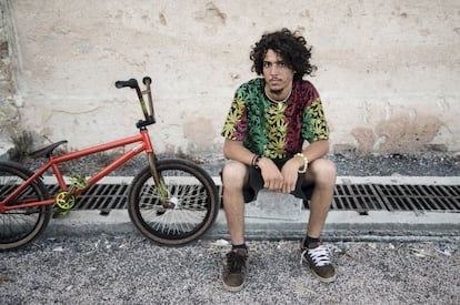 Los deportes por libre son una referencia internacional. Aquí, los de BMX. Estamos en la explanada del nuevo paseo fluvial, lugar de patinadores y demás. Allí acaba la muralla de la ciudad vieja y a su sombra descansa este chico. Todo en él es intencionado: la bicicleta con el naranja de las barras y el amarillo de los pedales, el blanco de los radios de una rueda y el negro de la otra. Él, a su vez, tiene los cordones de distinto color haciendo juego con sus muñequeras, una de ellas conjuntada con el collar. Pero lo que más destaca es la camiseta vegetal tricolor que internacionalizó Bob Marley.