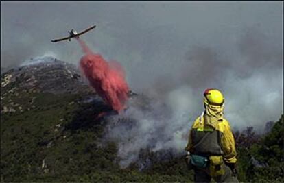 Un avión descarga agua sobre el fuego ayer en lo alto del Turmell, en Xert, ante la mirada de un bombero forestal.