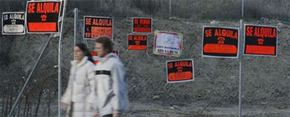 Una pareja pasea ante una valla con carteles de pisos en venta y en alquiler en Madrid.