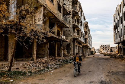 Un hombre pasa en bicicleta delante de unos edificios destruidos durante los combates de 2018 en el distrito de Bosra.