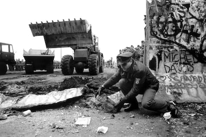 Un agente fronterizo de la República Democrática de Alemania mueve trozos del muro de Berlín ya en parte derribado. Detrás, se ven máquinas excavadoras con las que se han derrumbado las grandes losas que formaban la pared.