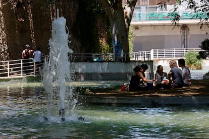 Unos jóvenes se reúnen bajo la sombra de un árbol y al lado de una fuente en el parque de la España Industrial en el barrio de Sants en Barcelona, este domingo.