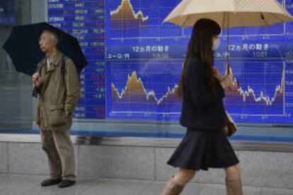 Una viandante pasa delante de una pantalla que muestra valores bursátiles en Tokio (Japón). La Bolsa de Tokio abrió hoy con una subida en su índice Nikkei del 0,81 por ciento. EFE/Archivo