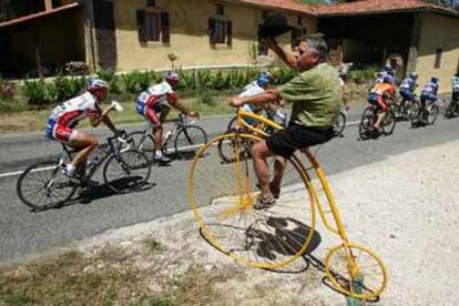 Un aficionado, montado en una original bicicleta, saluda a  los corredores con un sombrero en la mano.