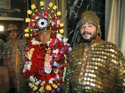 Dos hombres con trajes confeccionados con monedas y un tercero cubierto de flores en el salón del Sorteo.
