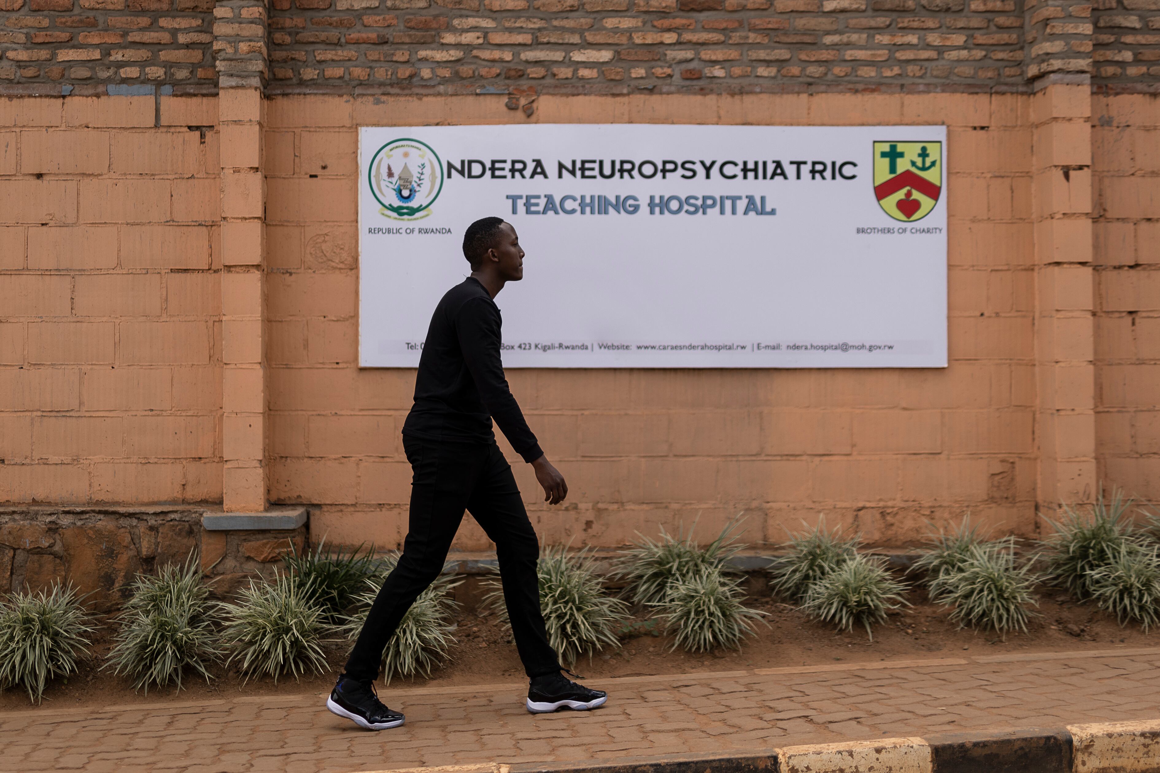 Un hombre camina junto al cartel de la entrada principal del hospital geropsiquiátrico Ndera, en la capital ruandesa. Aunque el Gobierno se ha esforzado por descentralizar los servicios de salud mental, de forma que lleguen hasta el último rincón del país, este centro médico sigue siendo la referencia en la materia y el lugar al que son trasladados los enfermos más graves. De ahí, el estigma que sigue rodeando al lugar.