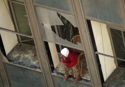 Un hombre, sentado delante de un ventana rota, observa los disturbios en la calle desde un edificio de la Universidad Americana en El Cairo