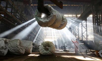 Un trabajador dirige una grúa que levanta alambres de acero en una fábrica en Dalian (China).