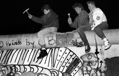 Tres jóvenes, dos de ellos con un martillo y un pico, golpean el Muro de Berlín durante su caída, en la República Democrática de Alemania.