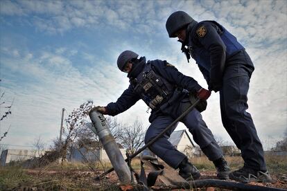 Dos empleados del cuerpo de los Servicios Estatales de Emergencias de Ucrania tratan de retirar un misil incrustado en un camino de Kutuzivka (región de Járkov)