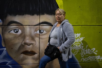 Teresa Gómez, madre buscadora del colectivo Mujeres Caminando por la Verdad, es retratada al lado del rostro pintado de su hijo desaparecido, Herney Mejía, en el nuevo mural en Medellín, el 15 de enero de 2025.