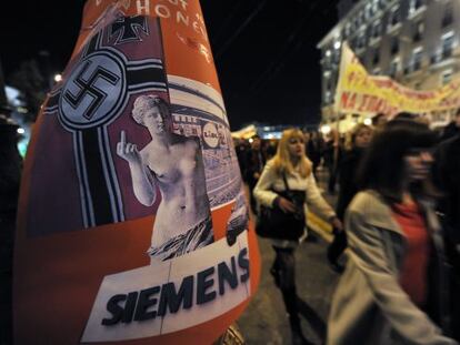 Un grupo de manifestantes pasa junto a un cartel cr&iacute;tico con una publicaci&oacute;n alemana antigriega. 