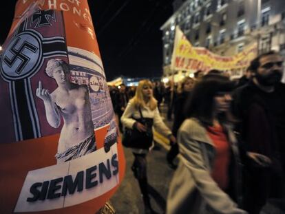 Un grupo de manifestantes pasa junto a un cartel cr&iacute;tico con una publicaci&oacute;n alemana antigriega. 