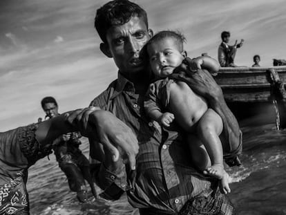 Un refugiado rohingya lleva en sus brazos a un bebé después de llegar en barco a Bangladesh después de huir de su pueblo en Myanmar, el 1 de octubre de 2017 en Cox's Bazar, Bangladesh.