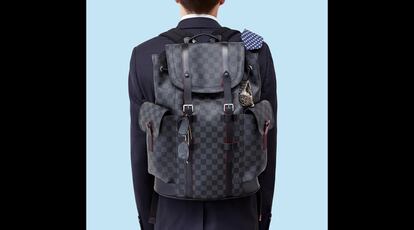 Mochila modelo Christopher PM de Louis Vuitton en lona Damier Graphite (cuadros de damero en negro y gris). De las hebillas cuelgan un reloj en cerámica de plasma de Rado y unas gafas Ray-Ban. El traje azul oscuro es de Dior; la camisa blanca, de Caramelo, y la corbata de lino, de Forecast.