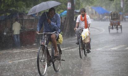 Varios hombres indios andan en bicicleta bajo la lluvia en Allahabad, en plena temporada del monzón en la India.