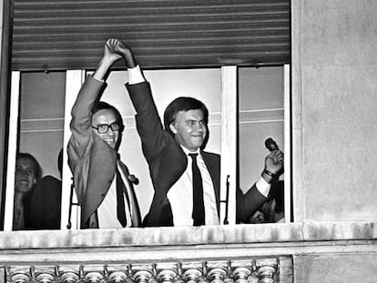 Alfonso Guerra levanta la mano de Felipe Gonz&aacute;lez, asomados ambos a una ventana del hotel Palace de Madrid, celebrando la hist&oacute;rica victoria del PSOE en las elecciones de 1982.  
 