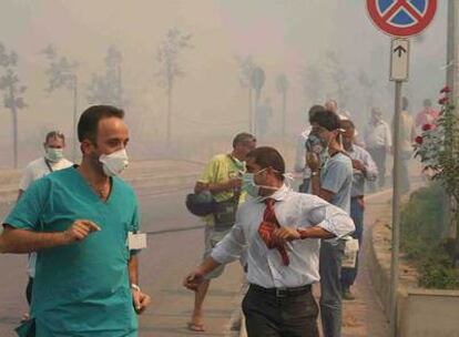 Decenas de personas se protegen del humo con mascarillas al ser evacuadas de un hospital de Cefalú.