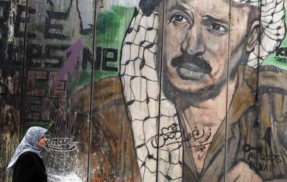 Una mujer camina frente a un mural con el rostro del fallecido líder palestino Yasir Arafat, en Ramala.