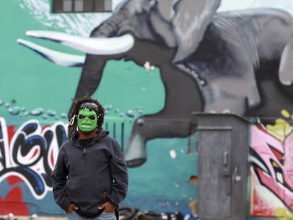 Un hombre con una máscara frente a un graffiti en Woodstock, un suburbio de Ciudad del Cabo.