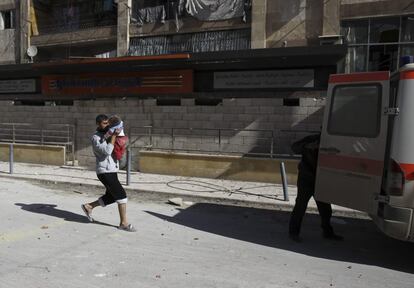 Un hombre con un bebé en brazo corre hacia una ambulancia tras un bombardeo en el barrio de Al-Ansari en Alepo (Siria), 31 de enero de 2014.