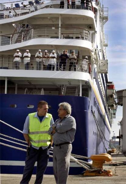 Dos personas conversan ante un barco atracado en el puerto de Valencia.