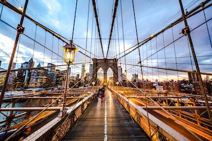 Con sus torres gemelas de arcos y gruesos cables geométricos, el famoso (y cinematográfico) puente de Brooklyn tiene un pasado algo tenebroso: 27 hombres fallecieron durante su construcción, entre 1869 y 1883. Actualmente, se reconoce tanto su esfuerzo como la perspicacia del arquitecto John Roebling, que estimó la necesidad de incorporar un gran paso peatonal a la estructura: a finales del siglo XIX la única forma de cruzar el East River entre Nueva York y Brooklyn (entonces ciudades independientes) era en ferri. Al inaugurarse fue el primer puente suspendido mediante cables de acero y durante 20 años se mantuvo como el más largo del mundo en su categoría. Hoy es una de las estampas más icónicas de Nueva York, por delante del puente de Manhattan o el de Verrazano-Narrows, que conecta Brooklyn con Staten Island; el de Queensboro, que une el Upper East Side de Manhattan con Long Island, en Queens; el de George Washington, que cruza el río Hudson (al oeste de Manhattan) hacia Nueva Jersey, o el puente de Williamsburg. <a href="https://www.brooklynbridgepark.org/" target="_blank"> El Brooklyn Bridge Park,</a> en Brooklyn, acoge sesiones de cine al aire libre en las noches de verano, con Manhattan y el puente como telón de fondo.