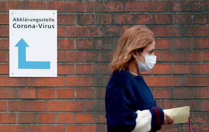 A woman, wearing a face mask, walks past a sign guiding people to the entrance of a corona testing station at the Vivantes Wenckebach hospital in Berlin on March 13, 2020. - German Chancellor Angela Merkel called on organisers of non essential events gathering hundreds of people to cancel them to help slow the spread of coronavirus. The regional governments of Germany's 16 states will decide if they want to shutter school gates according to the local situation, Merkel said on March 13, 2020, adding that an option could be to bring forward April's Easter school holidays. (Photo by Odd ANDERSEN / AFP)