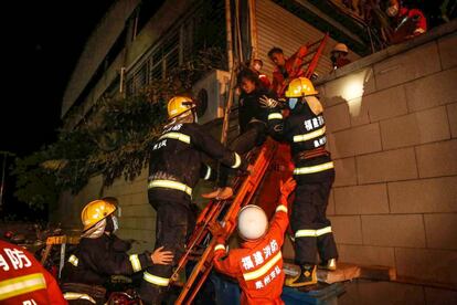 Una mujer baja por una escalera, ayudada por los bomberos, tras el derrumbe del edificio que albergaba al hotel derrumbado.