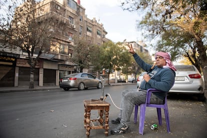 Un hombre fuma en un narguile, acompañado de su café, mientras hace la señal de la victoria en Damasco tras la caída del régimen de El Asad. 