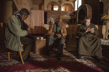 El en el salón de su casa de la ciudad de Palmira, el sectogenario Abdelmidan Al Rahim, acompañado de su vecino (centro) y hermano (izquierda), busca en su móvil las fotos que guarda de turistas llegados de todo el mundo a este oasis en tiempos de preguerra.