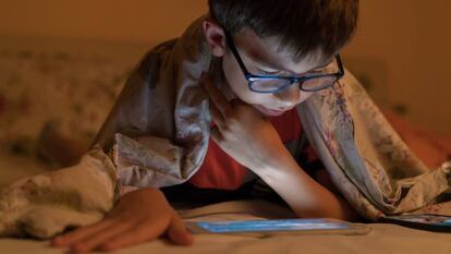 Un niño con  gafas mira un dispositivo.