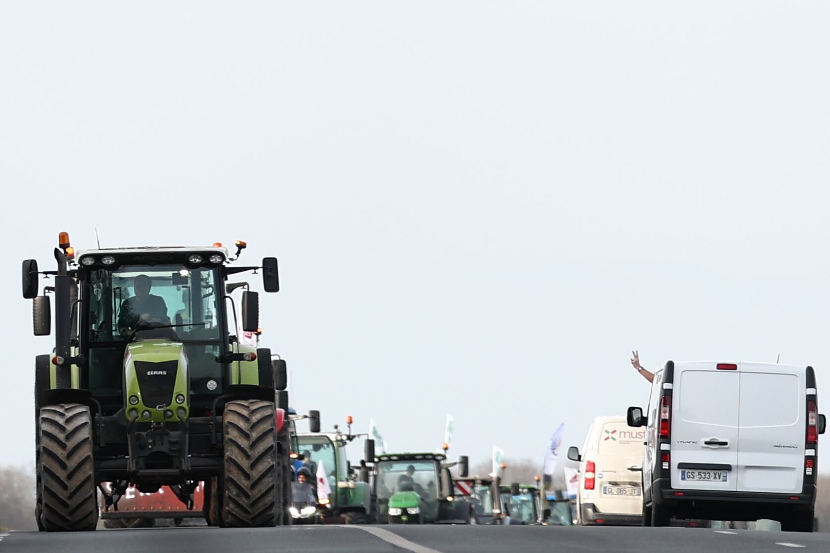 Un conductor hace el signo de la victoria desde su furgoneta mientras decenas de tractores llegan al punto de bloqueo de la carretera nacional D1001 cerca de Bornel, al norte de París.