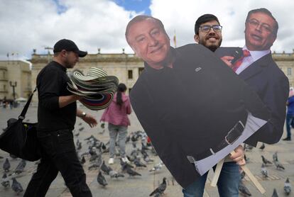 Un hombre posa sosteniendo carteles de cartón con imágenes de los candidatos a la Presidencia en Colombia en Bogotá.