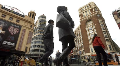 Personas pasan por delante del Palacio de la Prensa (derecha), en la plaza de Callao.