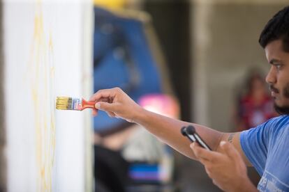 Em uma rua de Ramos, Pato faz os primeiros traços de uma nova pintura. Ele olha para a foto que vai copiar em seu smartphone ao mesmo tempo que rabisca com a mão direita na parede.