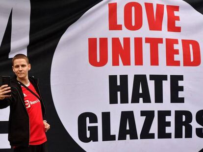 Un aficionado del Manchester United se fotografía junto a una pancarta que dice: 