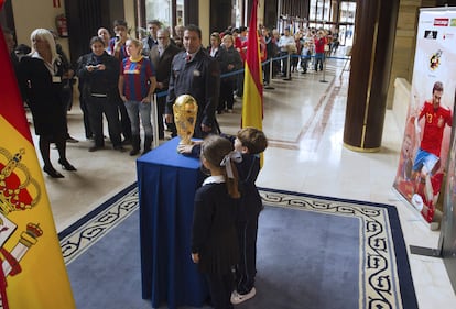 Dos niños observan la Copa del Mundo conquistada por la selección española de fútbol en el pasado mundial. El trofeo se presenta con motivo de la entrega del premio Príncipe de Asturias a los deportistas.