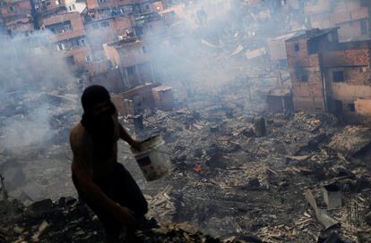 Un vecino de la favela de Paraisópolis corre con un cubo de agua para tratar de extinguir el incendio declarado en el lugar, en Sao Paulo (Brasil).