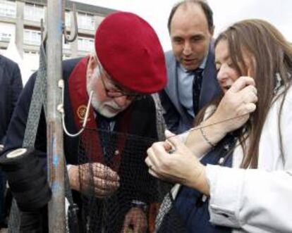 El candidato popular a las elecciones europeas, Miguel Arias Cañete (i), acompañado por el presidente cántabro, Ignacio Diego, observa como cose las redes una pescadora en la Feria, tras ser nombrado cofrade de honor de la Cofradia de la Anchoa, hoy en Santoña.