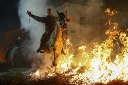 Un jinete pasa juntoa a las llamas de una hoguera a lomos de su caballo.