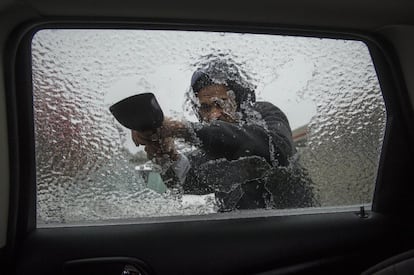 Un hombre trata de quitar el hielo que cubre la ventanilla de su coche, en Doraville